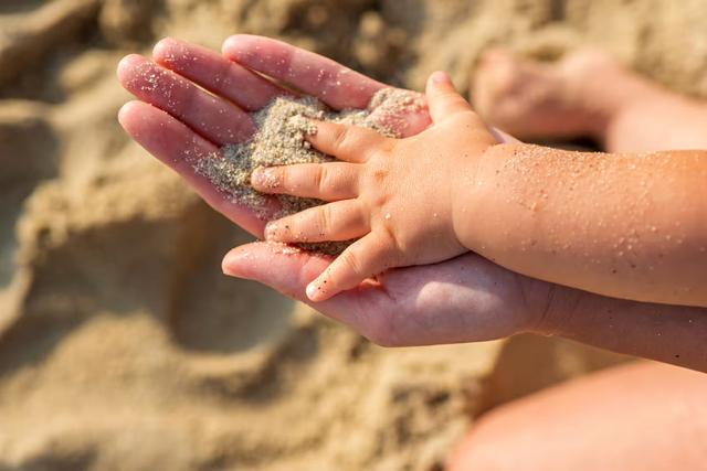 Mother and baby hands touching sand