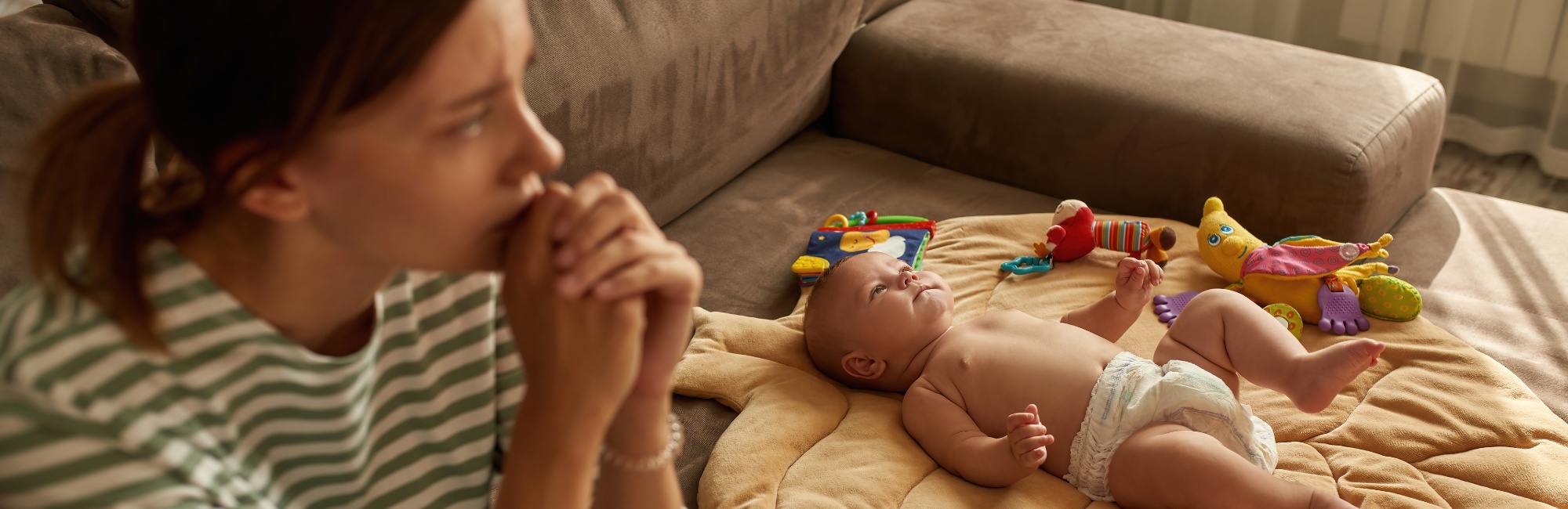 worried mother sits next to baby laying on its back